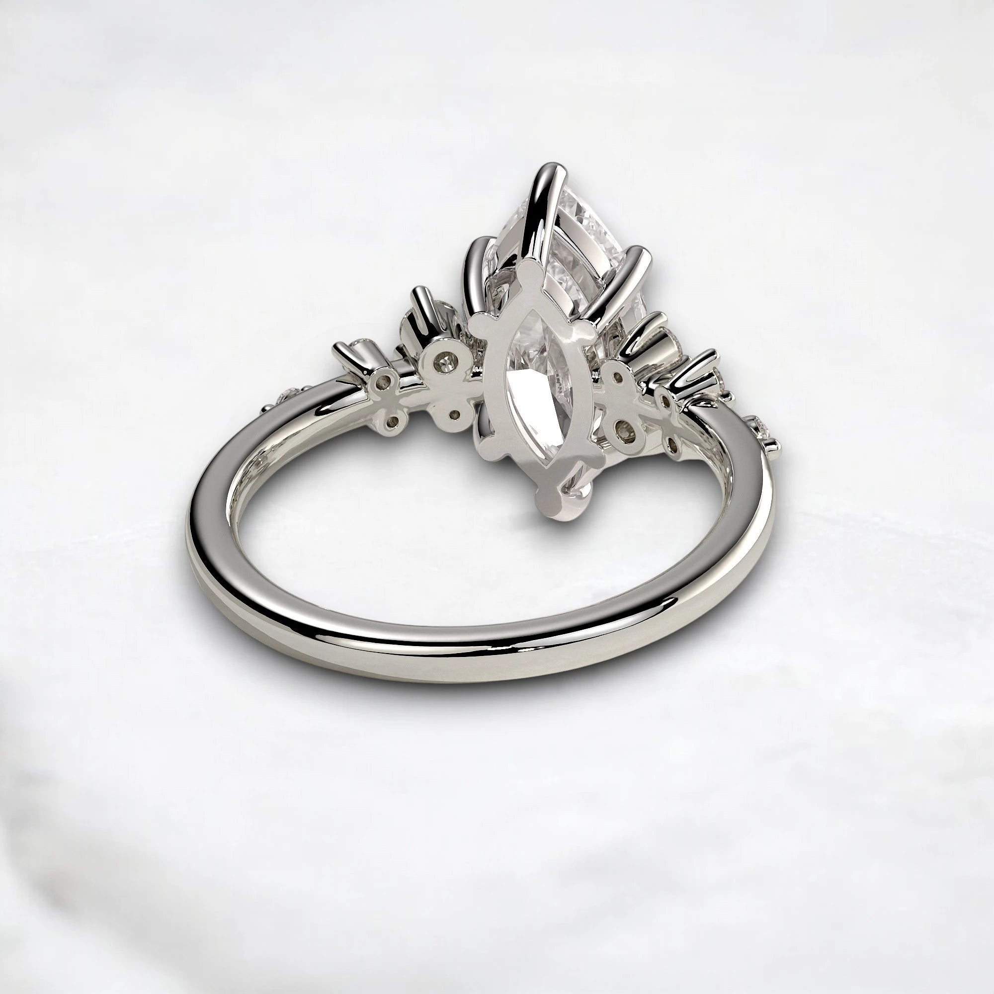 A silver ring featuring a marquise-cut clear gemstone in a decorative cluster setting, photographed on a light gray marble surface.