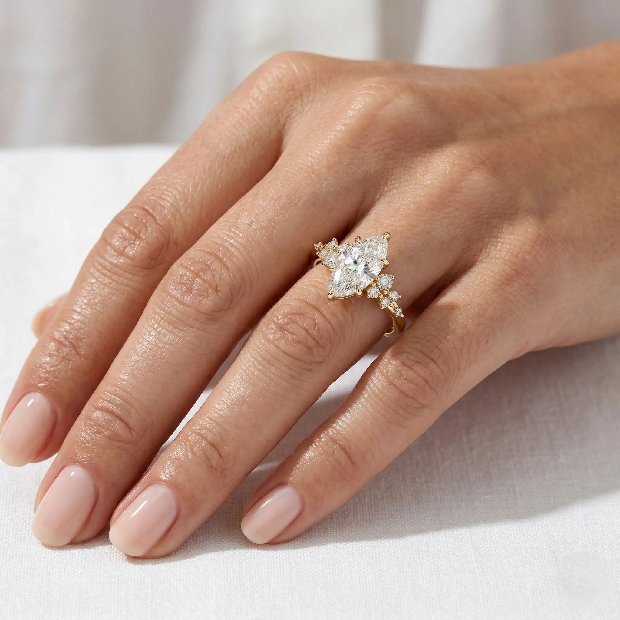 A close-up of a hand wearing a rose gold ring with a marquise-cut clear center stone and smaller side stones, resting on a white fabric surface.
