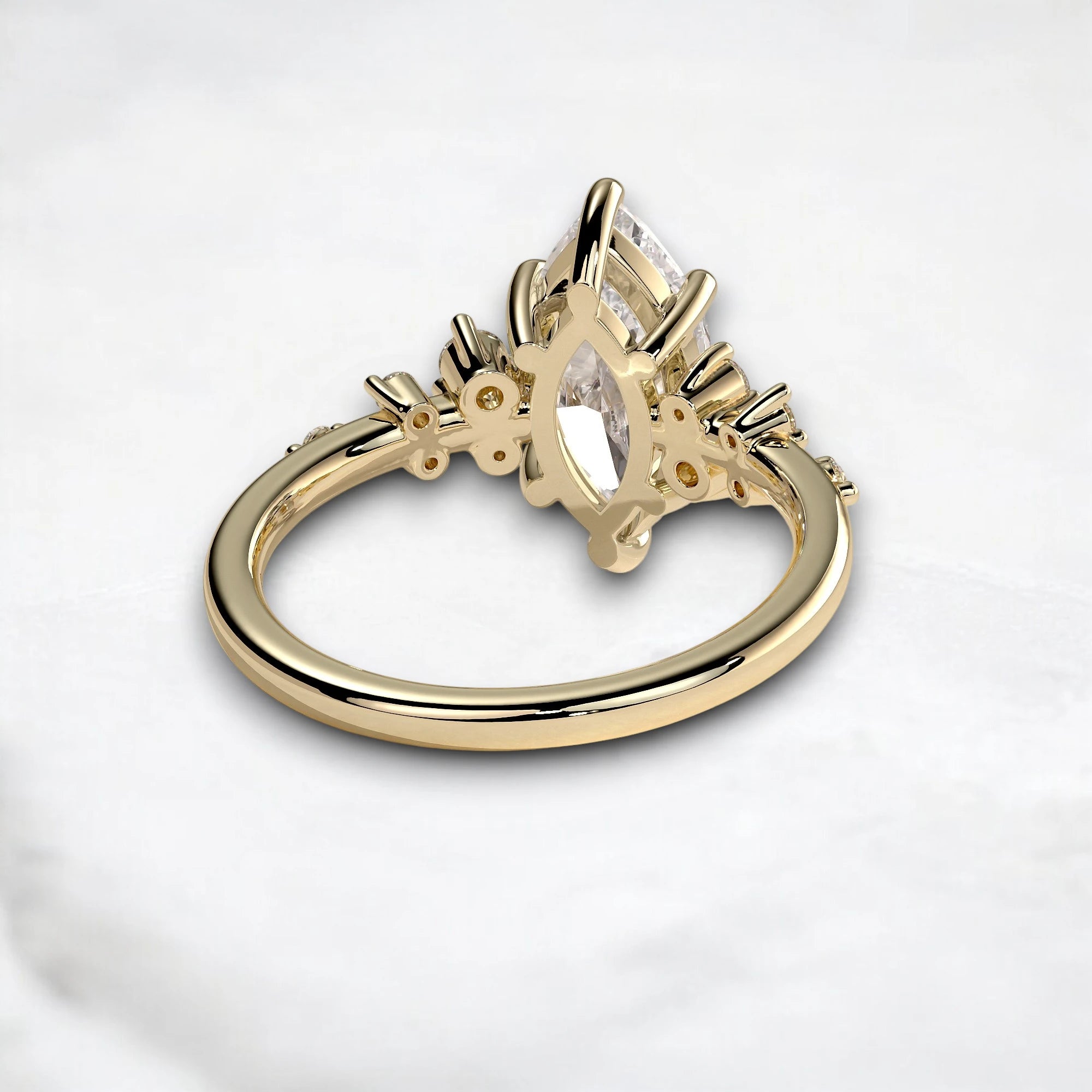 A gold ring with a marquise-cut clear gemstone in a decorative setting, photographed on a light marble surface.