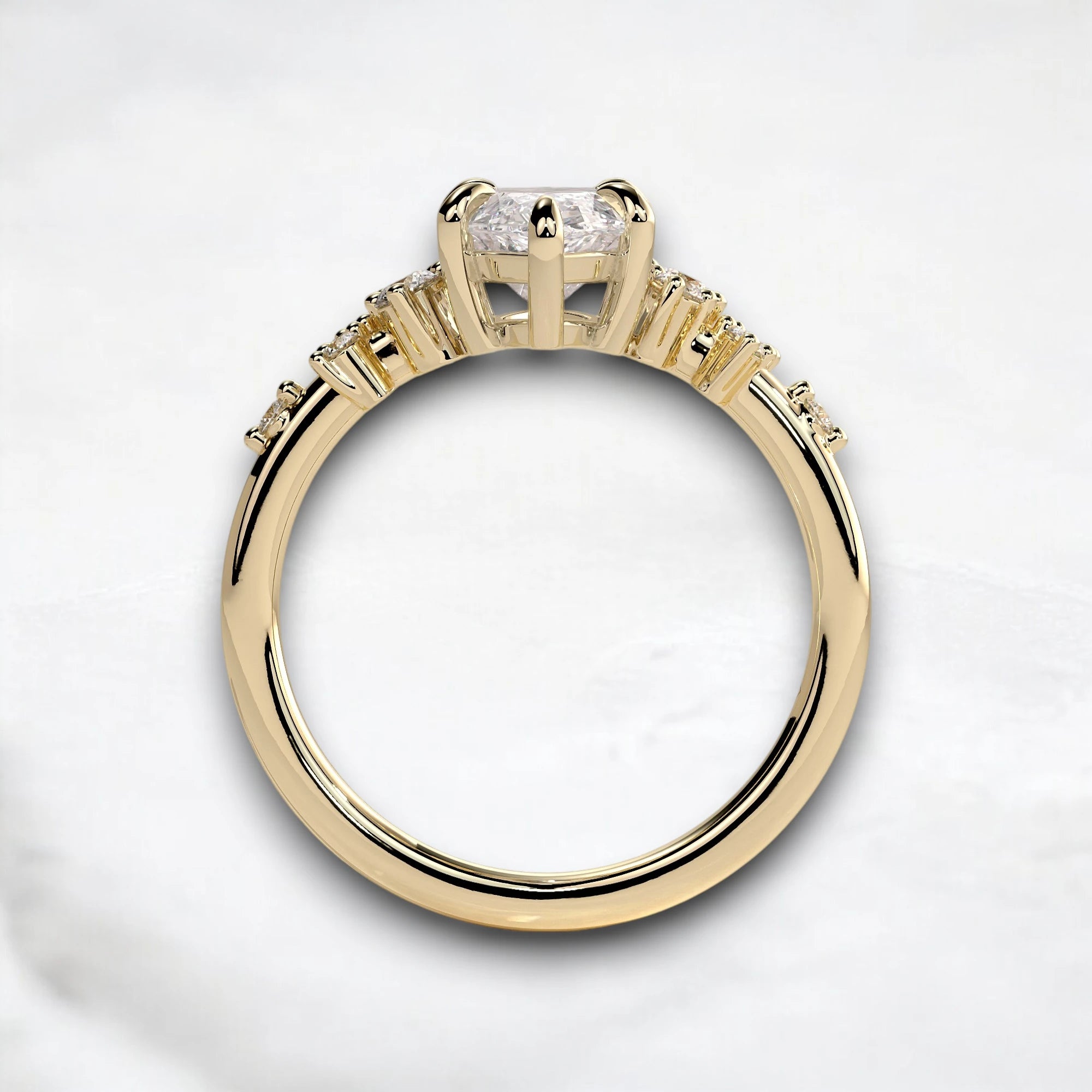 A yellow gold ring featuring a large round-cut diamond in a four-prong setting, with smaller diamonds set along the shoulders of the band, shown on a light gray marble background.