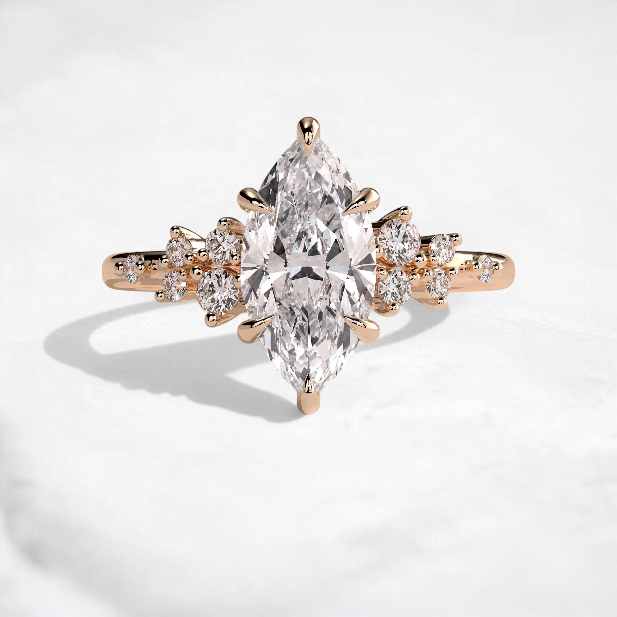 A rose gold ring featuring a large marquise-cut clear center stone with smaller round and pear-cut stones along the shoulders, photographed on a clean white surface.