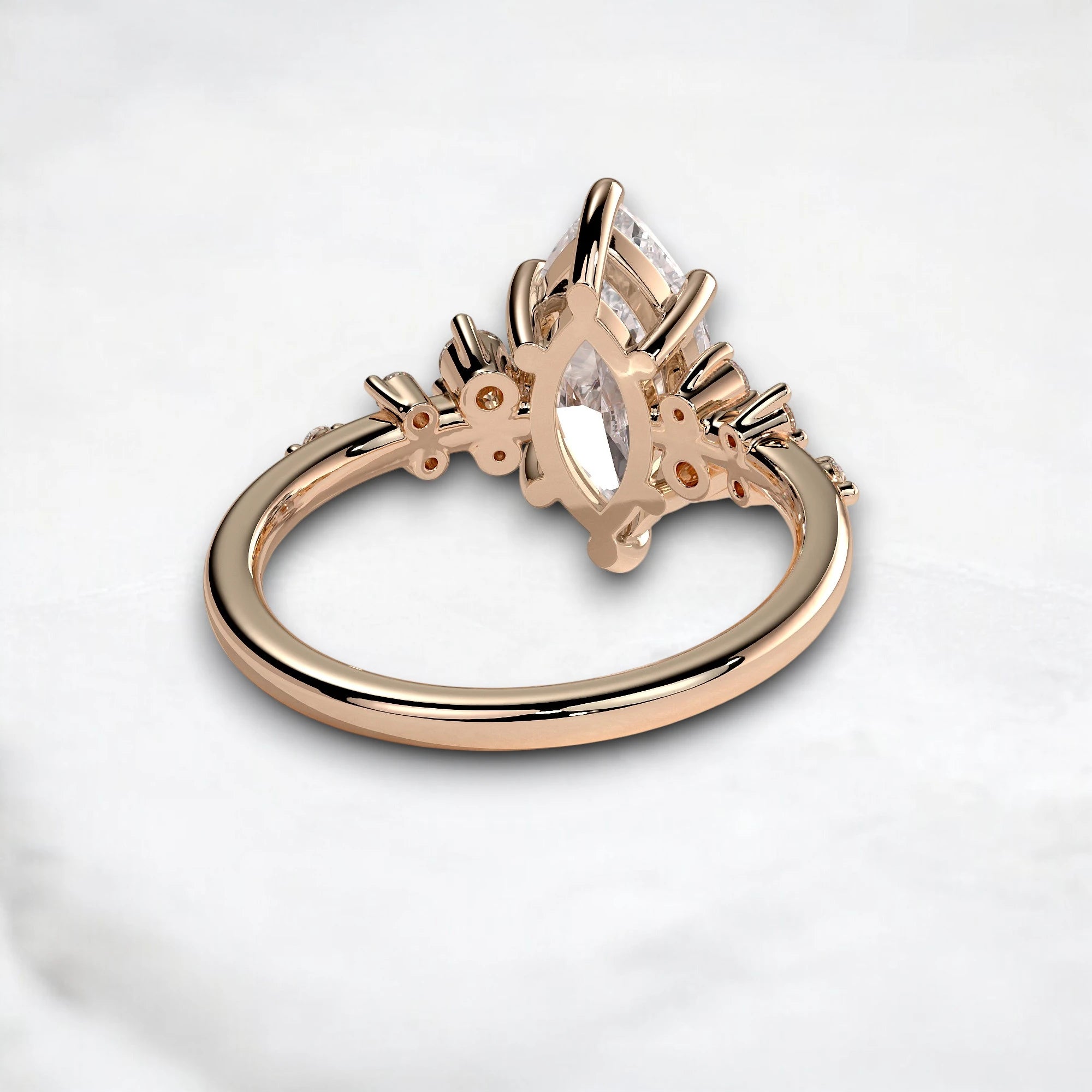 Rose gold ring with a marquise-cut clear gemstone in a detailed floral setting, photographed on a light marble surface.