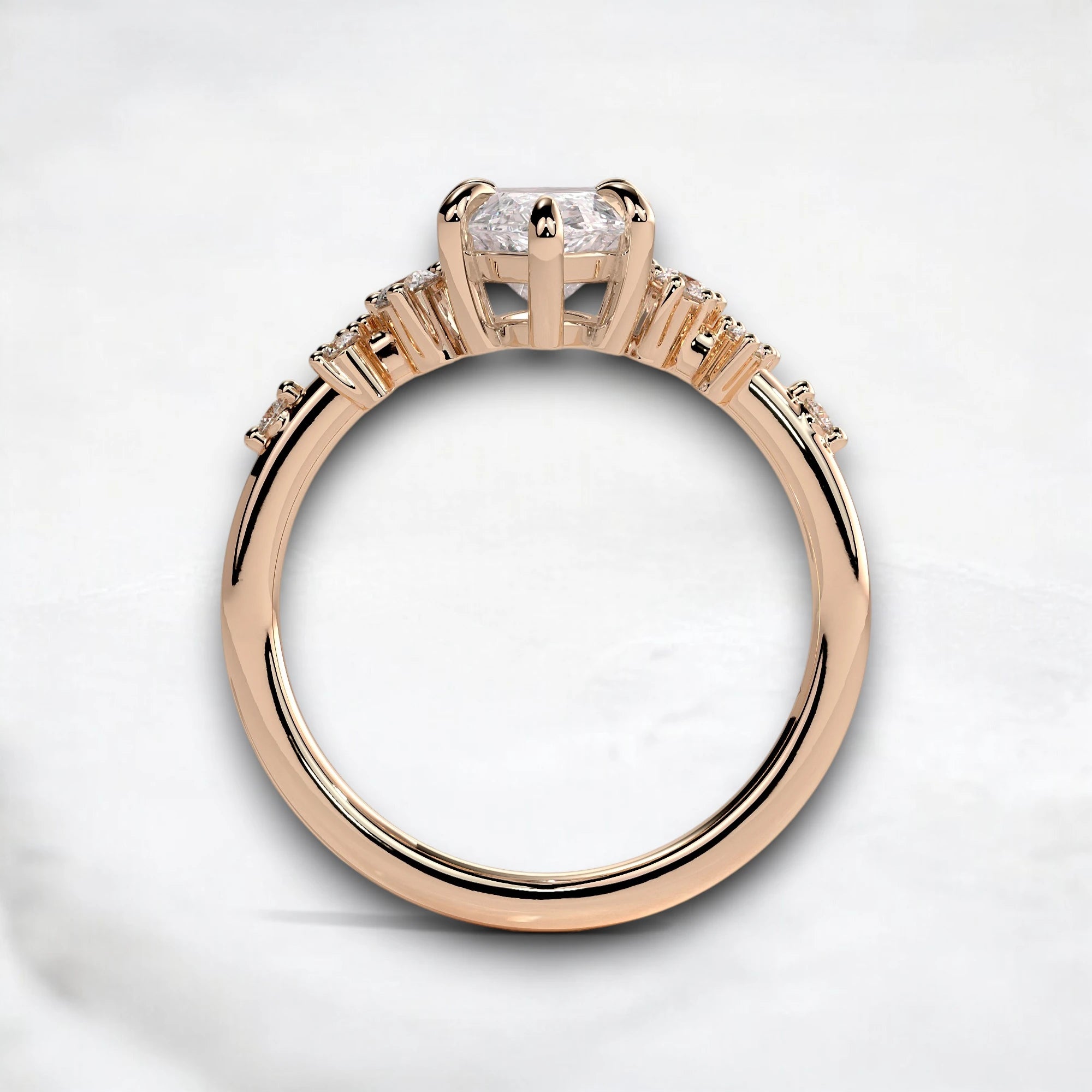 A rose gold ring with a large clear round-cut center stone and smaller side stones, shown from a top-down view on a light gray background.