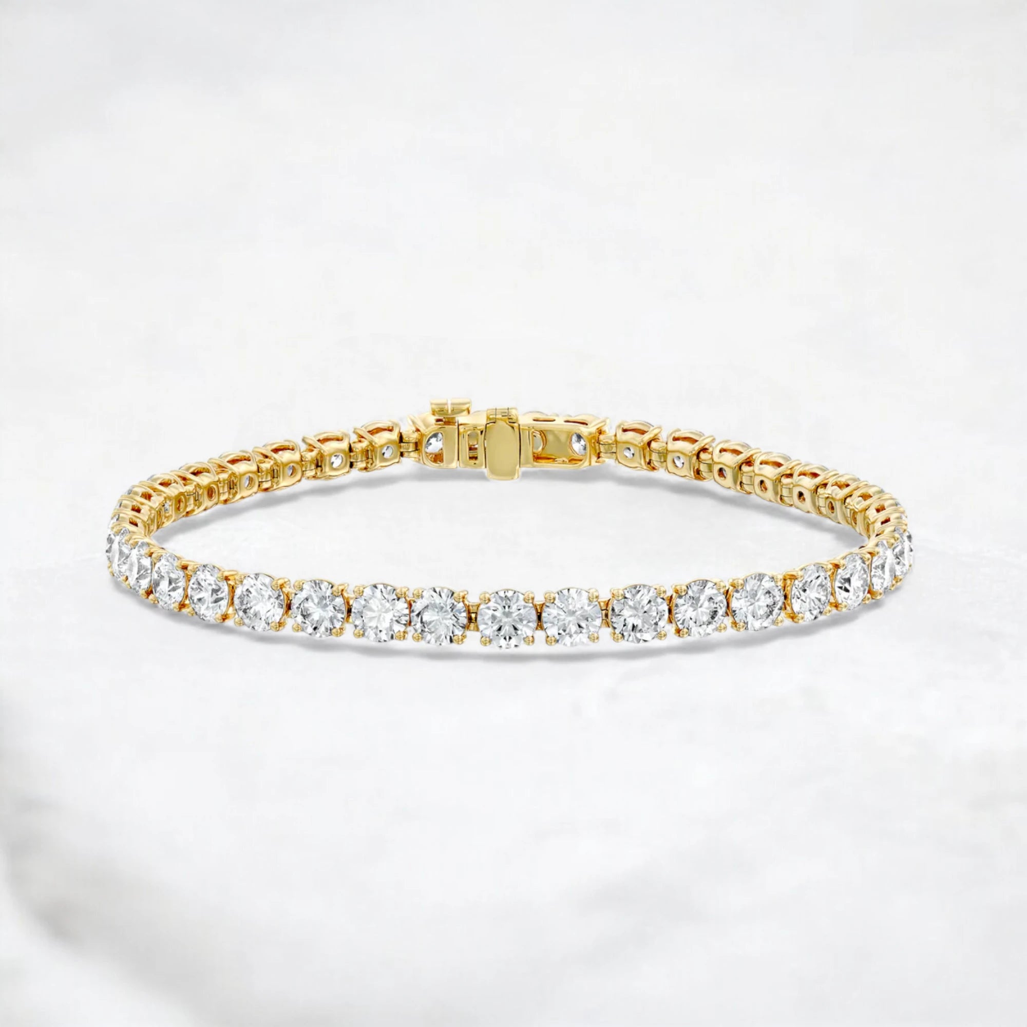 A yellow gold tennis bracelet featuring a row of round-cut clear gemstones, displayed on a light gray marble surface.