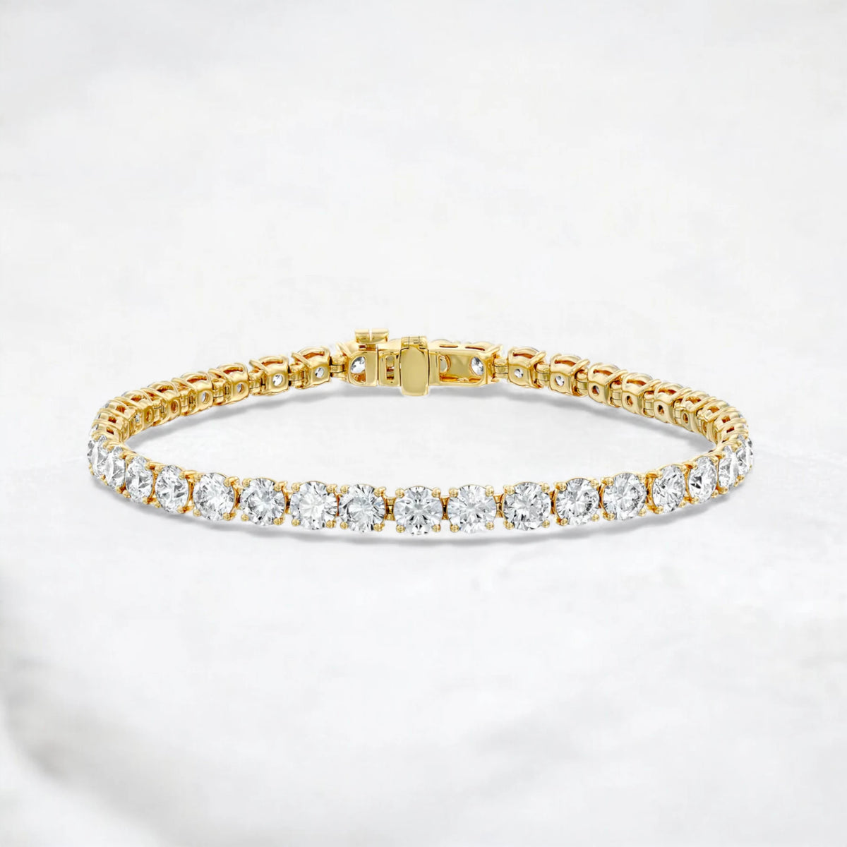 A yellow gold tennis bracelet featuring a row of round-cut clear gemstones, displayed on a light gray marble surface.