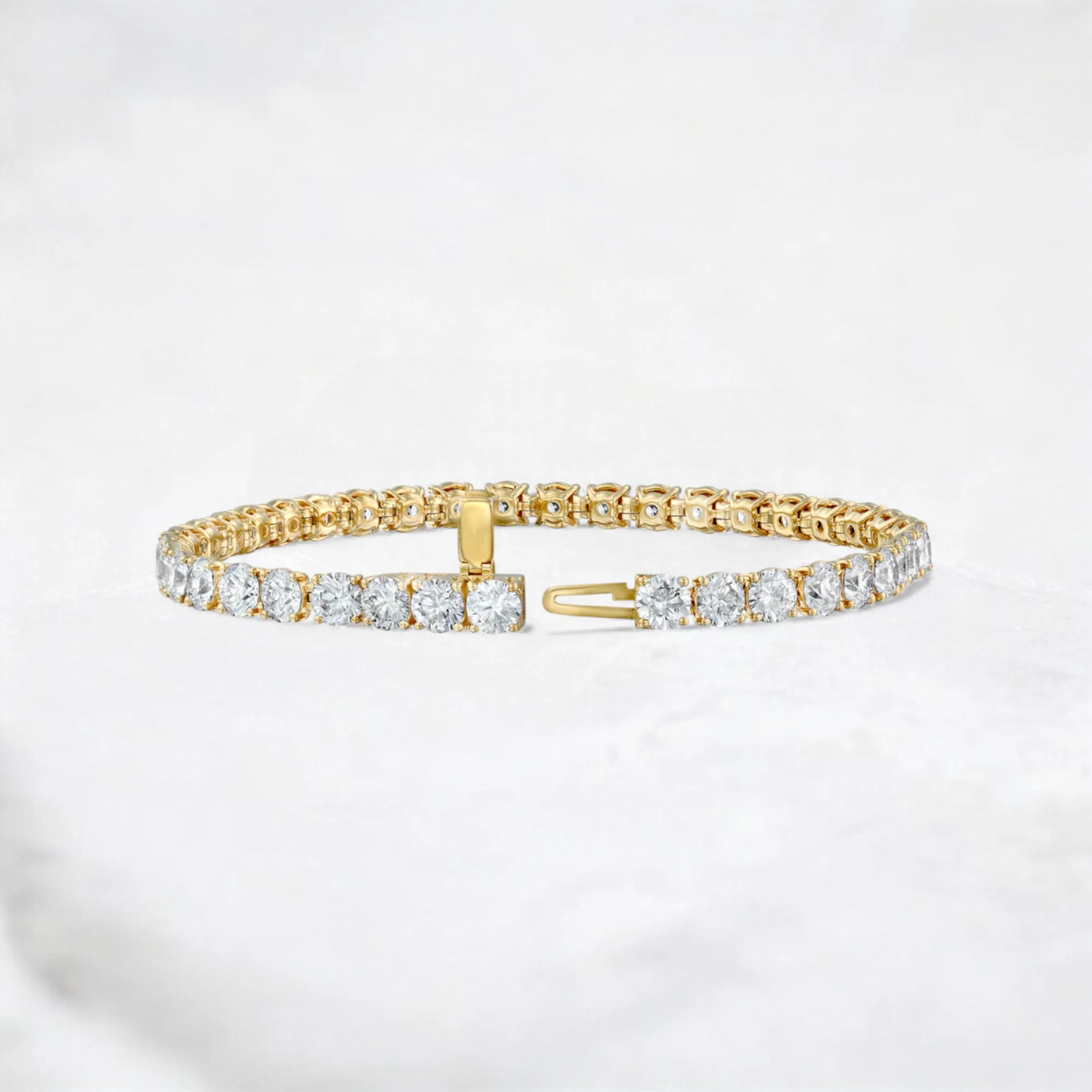 A gold tennis bracelet with clear round-cut gemstones, displayed on a light gray marble surface.