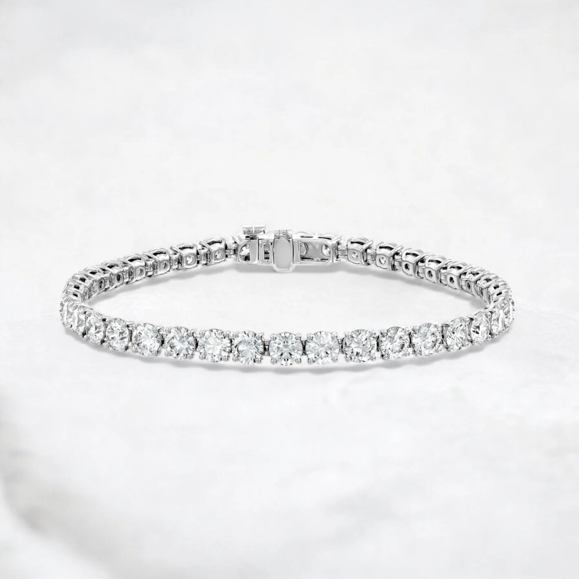 A silver tennis bracelet with a row of round-cut clear gemstones, displayed on a soft white textured background.