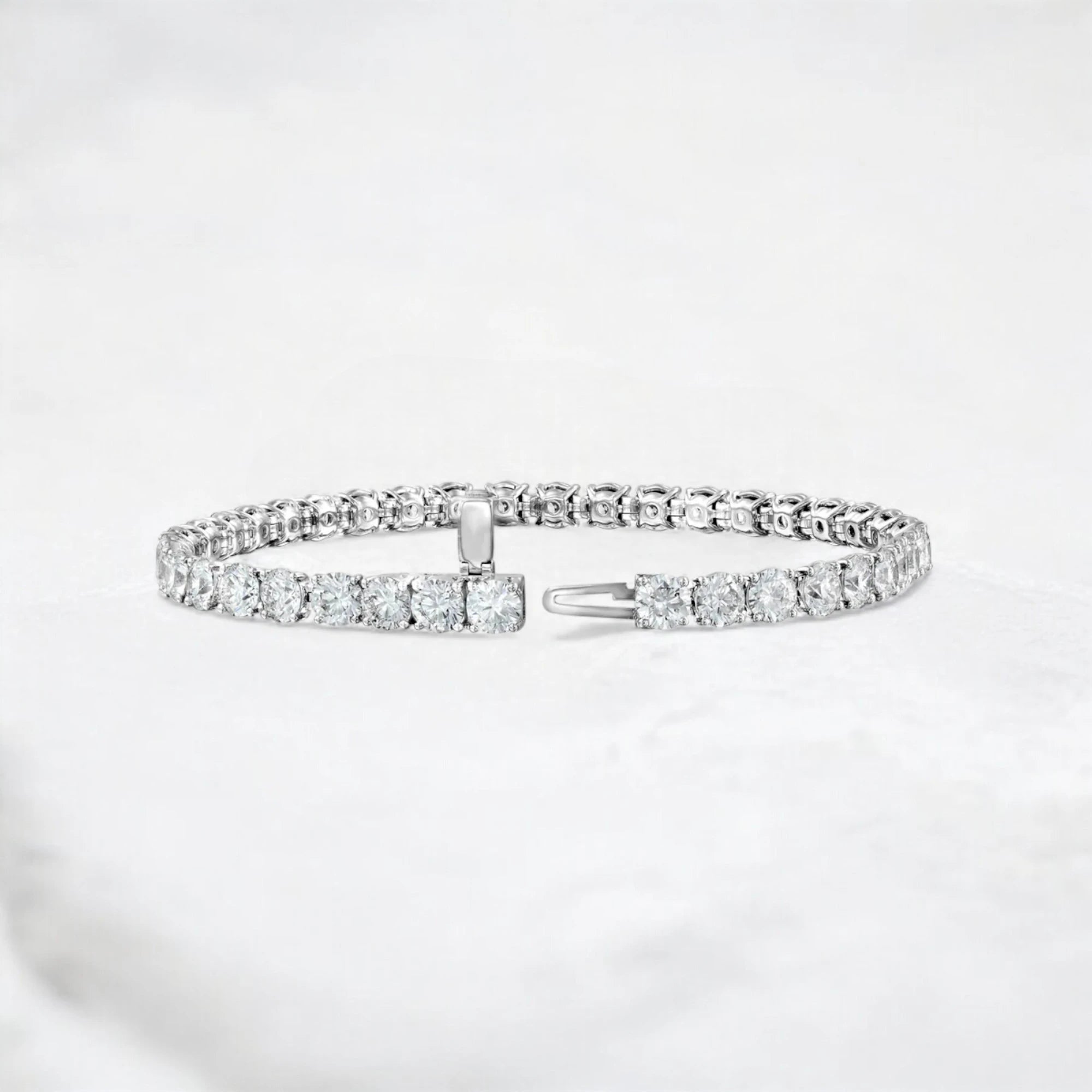 A silver-toned tennis bracelet with a row of clear rectangular gemstones and a sliding clasp, displayed on a soft white textured surface.