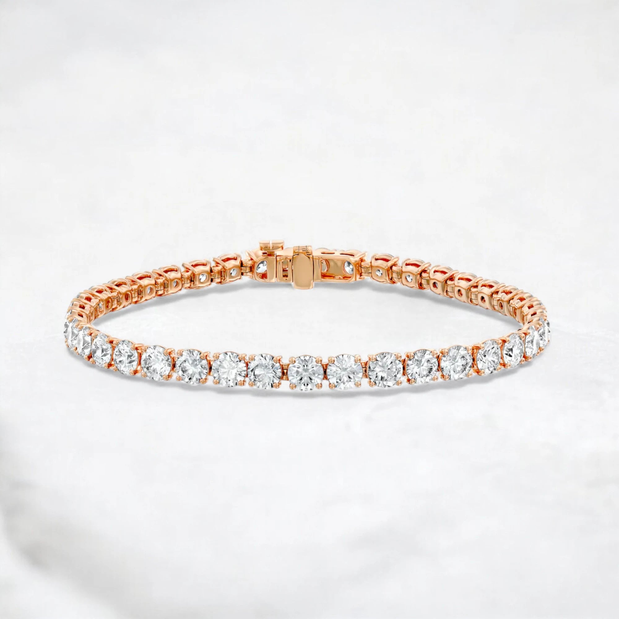 A rose gold tennis bracelet with round-cut clear gemstones, displayed on a light gray marble surface.