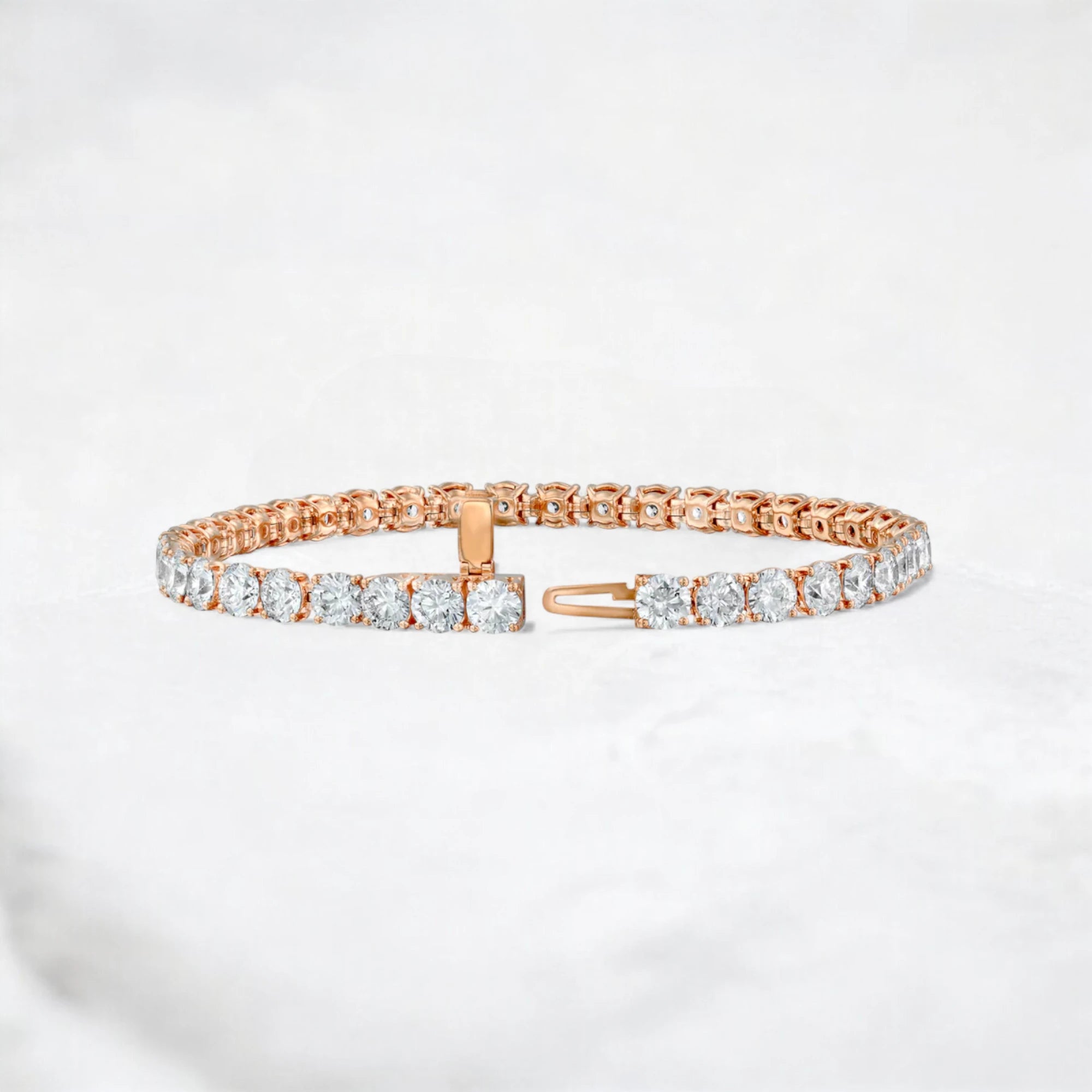 A rose gold tennis bracelet with clear round-cut gemstones, displayed on a light gray marble surface.